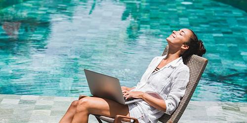 Woman sunning herself by the pool while working on a laptop